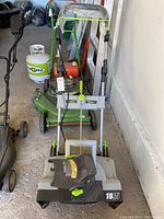 Front view of the snow thrower showing handle with control cables and 18 inch width marking on the snow clearing intake.