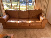 Front-facing view of a brown leather sofa showing three seat cushions and three back cushions with rounded armrests and visible wear.