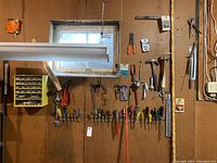 Wide shot of pegboard displaying assorted handtools including clamps, hammers, screwdrivers, pliers, and adjustable wrenches hung in an organized manner.