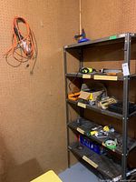 Corner metal shelving unit with various hand tools and orange extension cords hanging on pegboard wall.