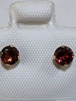 Front view of 10K yellow gold earrings with round garnet gemstones showing rich red color and faceted surface.