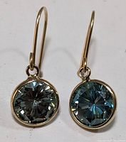Front view of 10K yellow gold earrings with round-cut blue-toned moissanite stones in bezel setting, showing both earrings side by side.