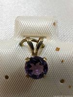 Close-up photo of round amethyst pendant set in 10K yellow gold on white textured background.