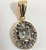Front view of the pendant showing the aquamarine center stone and surrounding clear stones in a yellow gold setting.