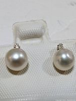 Front view of both earrings on white pad showing pearls and diamond accents