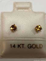 Front view of the pair of yellow sapphire stud earrings mounted on a white holder marked 14 KT. GOLD.