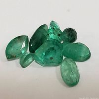 Top down view of 9 loose genuine emerald gemstones of various shapes and sizes.