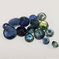 Multiple sapphire gemstones of various cuts and colors on white surface