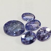 Five genuine loose tanzanite gemstones with blue to violet color hues, faceted oval cuts, and variable size.