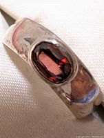 Close-up of sterling silver ring featuring an oval garnet stone from an angled view showing band surface details and gemstone color.