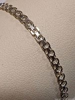Close-up of sterling silver linked bracelet showing detailed link design on a textured white background.