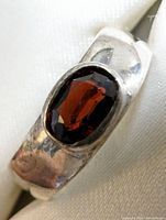Close-up front view of sterling silver ring with oval garnet stone showing color and setting detail.