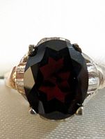 Close-up of front view of sterling silver ring with oval garnet gemstone showing facets and prong setting.