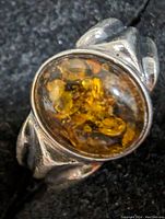 Close-up image of the sterling silver ring featuring an oval amber gemstone with natural inclusions, showing the front and side of the ring.