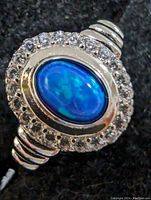 Close-up front view of sterling silver ring with an oval blue opalite center stone surrounded by small cubic zirconia stones.
