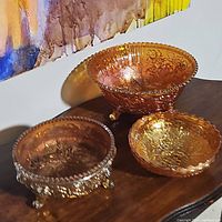 Three carnival glass bowls set on a wooden surface showing size and color variation