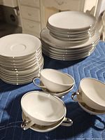 Stack of small plates and large plates with silver trim, along with tea cups on a cloth.