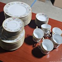 Full view of china set with stacked plates and cups showing floral and gold trim design.