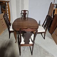 Full view of wooden dining table surrounded by four chairs in storage.
