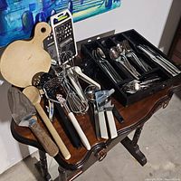 Overview of flatware, kitchen utensils, cutting boards, and gadgets on wooden table