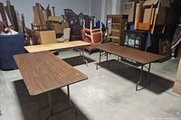 Three folding tables arranged in a U-shape in a storage area with other furniture items