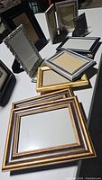 Photo of an assortment of 11 picture frames in various sizes and styles arranged on a gray table surface.