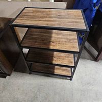 Full view of the three-shelf stand showing wood grain shelves and black metal frame