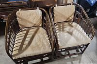 Pair of vintage rattan armchairs with tan cushions photographed side by side showing full-frontal view of frames and cushions.