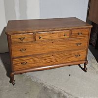 Front view of closed dresser showing wood grain, drawer configuration, and metal handles on wheels.