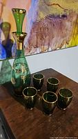 Green glass decanter with gold decorative accents and six matching glasses on wooden surface.