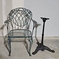 Front view showing wrought iron chair and separate table base on floor against white wall.