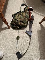 Full view of vintage compound bow laid on carpet with camouflage carrying case partially underneath