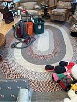 Full view of the braided oval rug laid on hardwood floor with household items on top to show scale and condition.