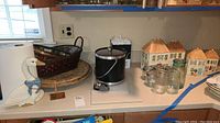 Multiple ceramic canisters shaped like houses, Mason jars, metal ice bucket, baskets, and woven trays on kitchen counter