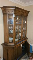 Full front-side view of oak china cabinet showing glass display doors containing glassware and lower closed wooden cabinet with door open.
