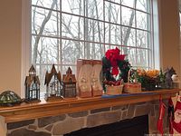 Wide view of mantel with three tea light lanterns, holiday wreath, baskets with faux greenery, and handcrafted tree toppers.