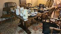 Full view of vintage wooden dining room table with various items placed on top (not included in sale). Shows table shape, top, and chairs around it.