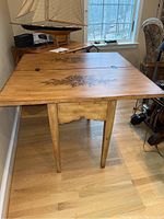 Full view of wooden flip top table with floral paintings on the top surface, closed position.