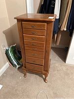 Front view of wooden jewelry chest showing seven front drawers with brass handles and curved legs.