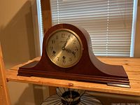Front view of the wooden mantle clock on a wooden surface, showing full case and clock face.