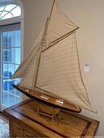 Full view of the large model sailboat, showing the cloth sails, wooden mast, and black hull on wooden stand.
