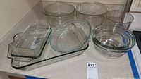 Multiple clear glass Pyrex cookware pieces including bowls, loaf pans, pie plate, and casseroles shown on a kitchen counter.