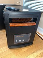 Front and side view of EdenPure portable heater with remote on top, showing black metal housing and wood-look accent grille.