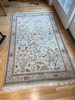 Full view of 3x5 area rug on hardwood floor, showing floral and vine design with a decorative border and cream-colored fringe.