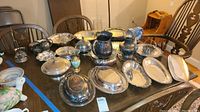 Photo showing full assortment of vintage silverplate items on a wooden dining table including serving trays, bowls, covered dishes, pitchers, candle holders, and a decorative vase.