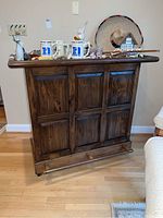 Front view of vintage wooden bar showing paneled front and casters.