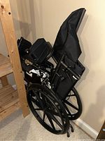 Portable folding wheelchair folded and leaning against wall next to wooden furniture.