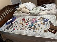 Wide view of the costume jewelry and scarves spread on white mattress showing the assortment of pins, necklaces, earrings, bracelets, and scarves.
