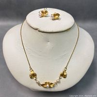 Front view of necklace and earrings displayed on white stand showing gold filled floral motifs with faux pearls