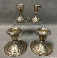 Two pairs of sterling silver candleholders displayed, one on an elevated clear stand showing height difference and base detail
